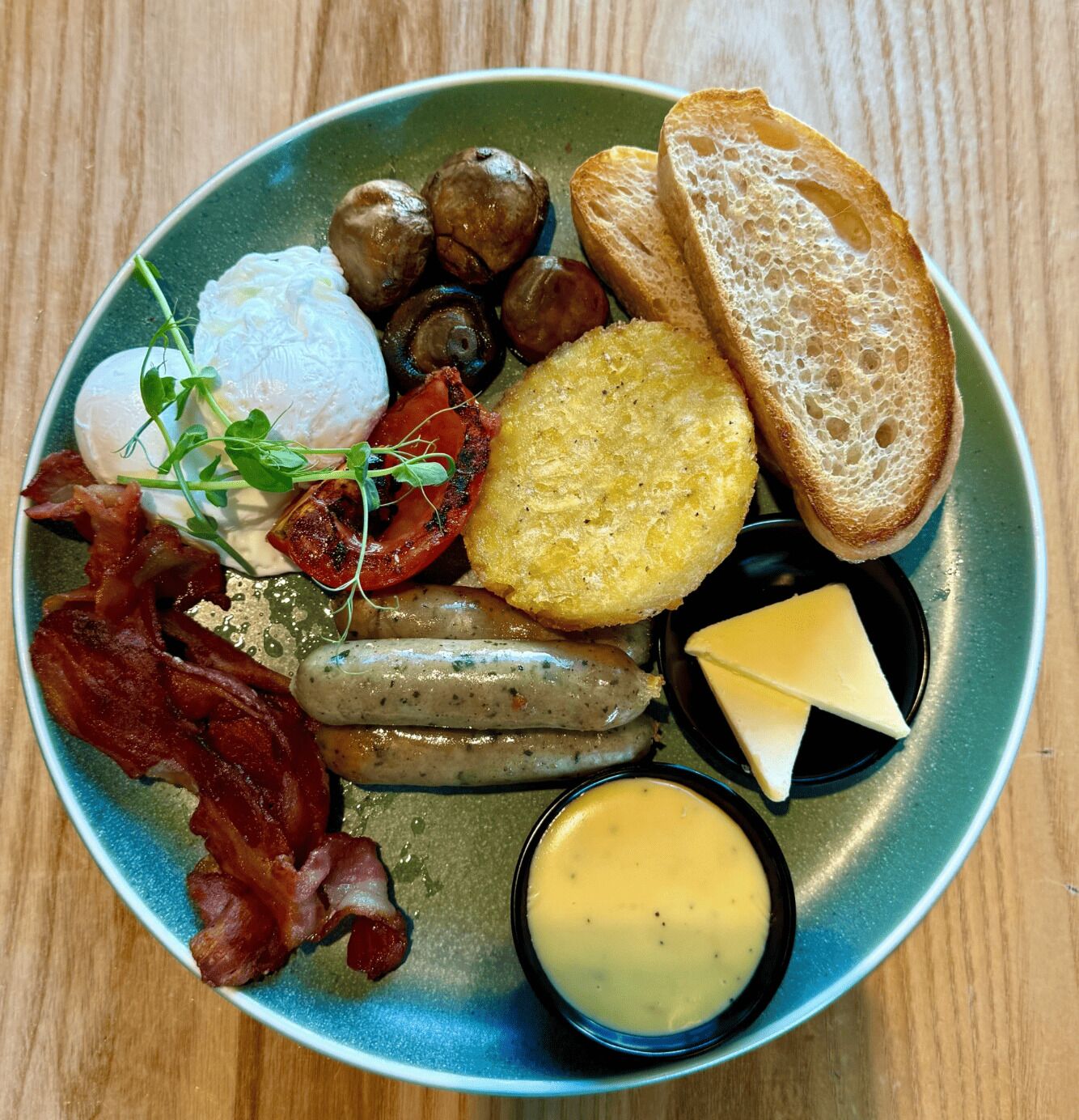 A plate of breakfast food including eggs, bacon, sausages, mushrooms, toast, and cheese.