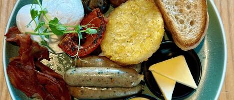 A plate of breakfast food including eggs, bacon, sausages, mushrooms, toast, and cheese.