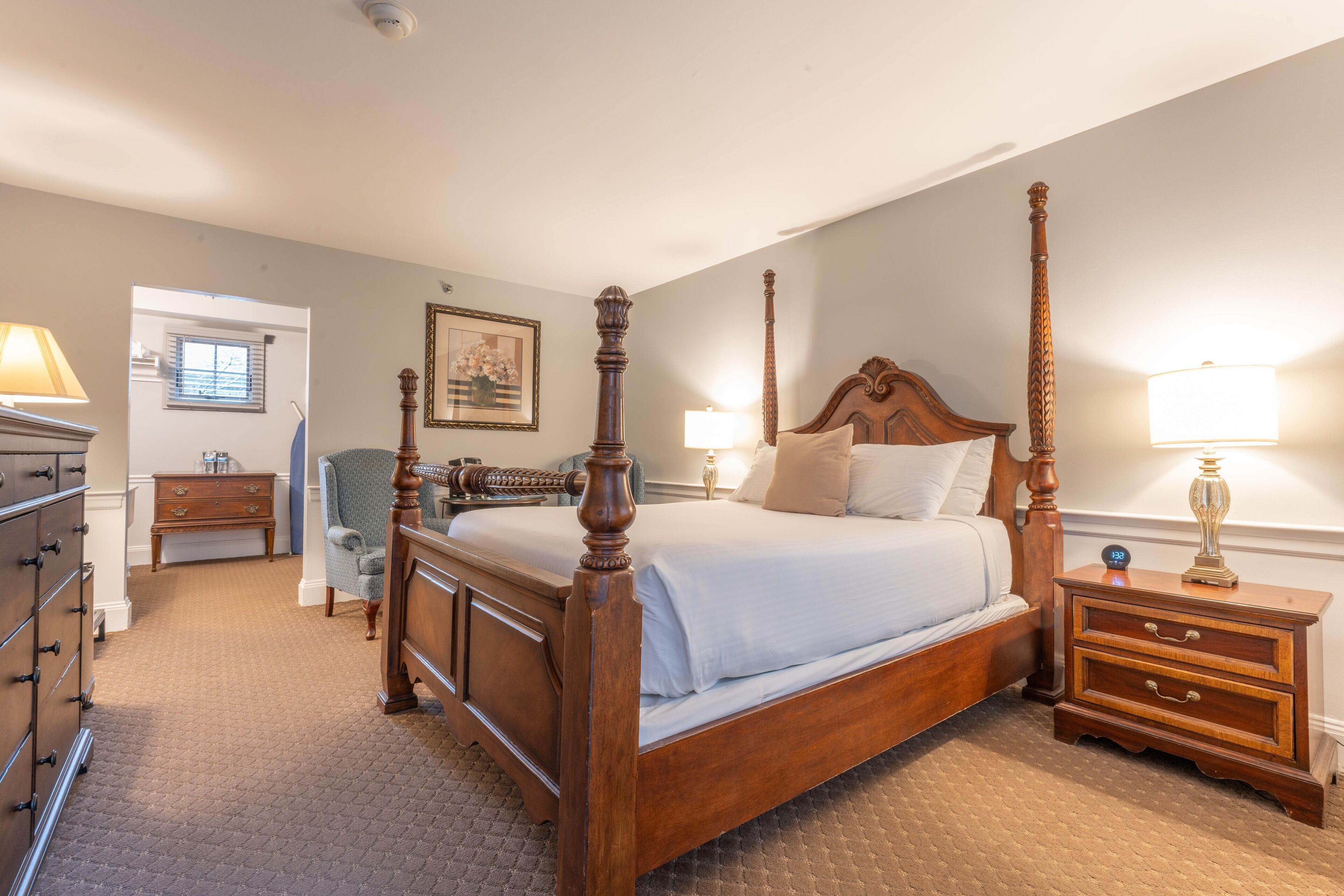 A four-poster bed with a wooden frame, a nightstand with drawers, a lamp, and a chair.