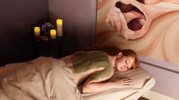 Una persona acostada en una cama con una manta verde, una mesita de noche con velas y un cuadro en la pared.