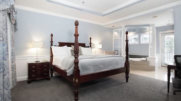 Een hemelbed met houten frame, een nachtkastje met lades, een bureau met stoel, en een groot raam met jaloezieën.