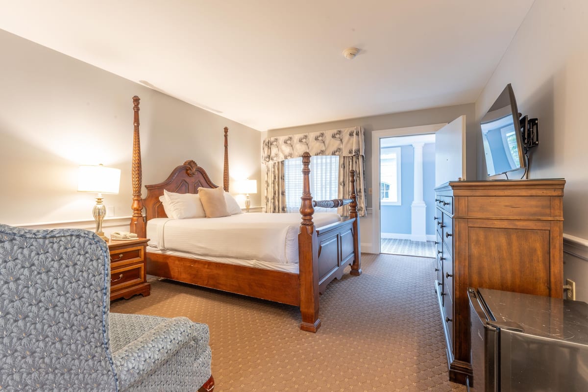 A bedroom with a four-poster bed, wooden dresser, and a television on the wall.