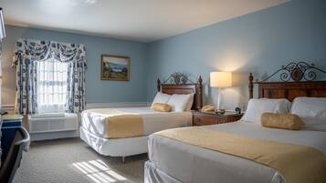 Une chambre d’hôtel avec deux lits, un bureau, une chaise, une lampe et un tableau au mur.