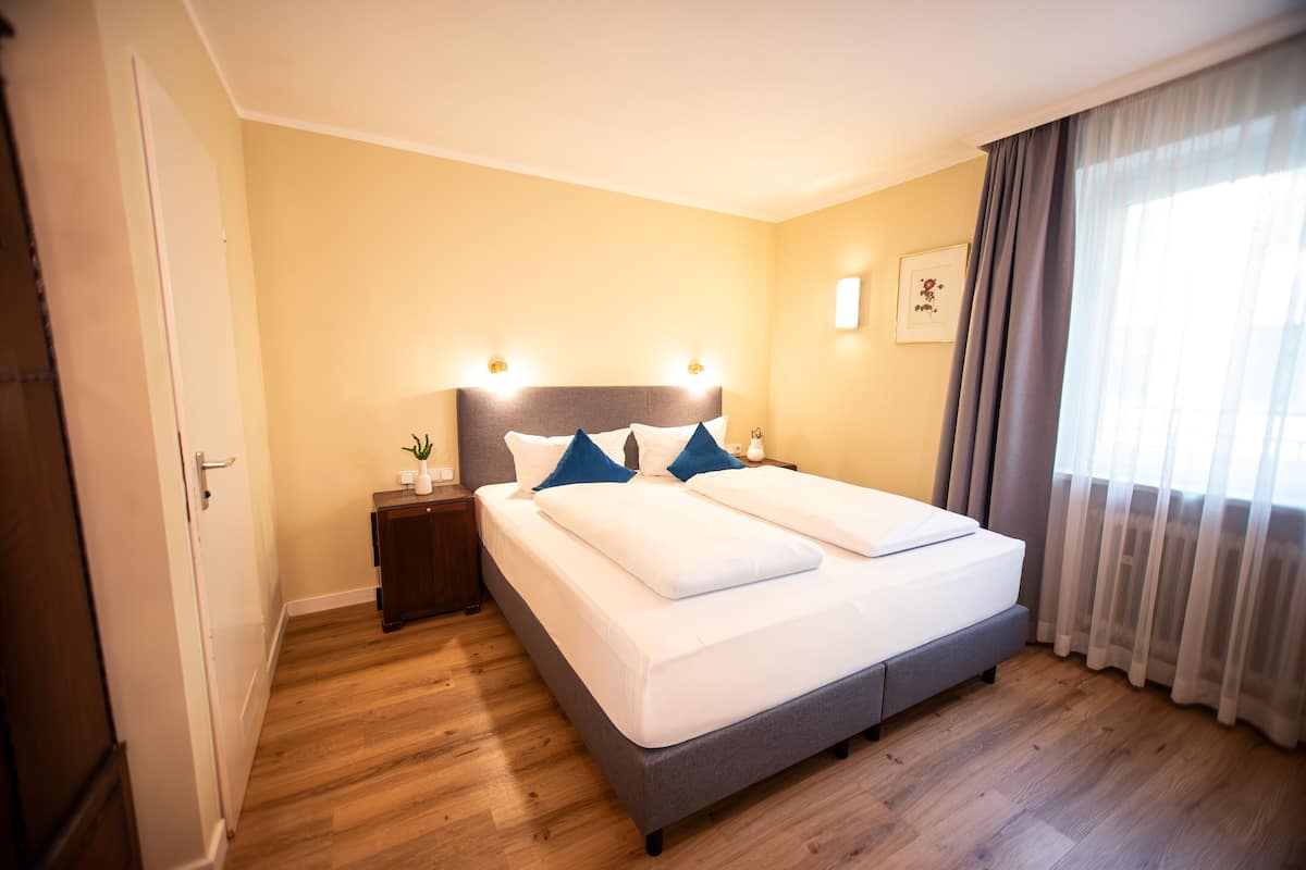 A double bed with a grey headboard, two bedside tables, a small nightstand, and a framed picture on the wall.