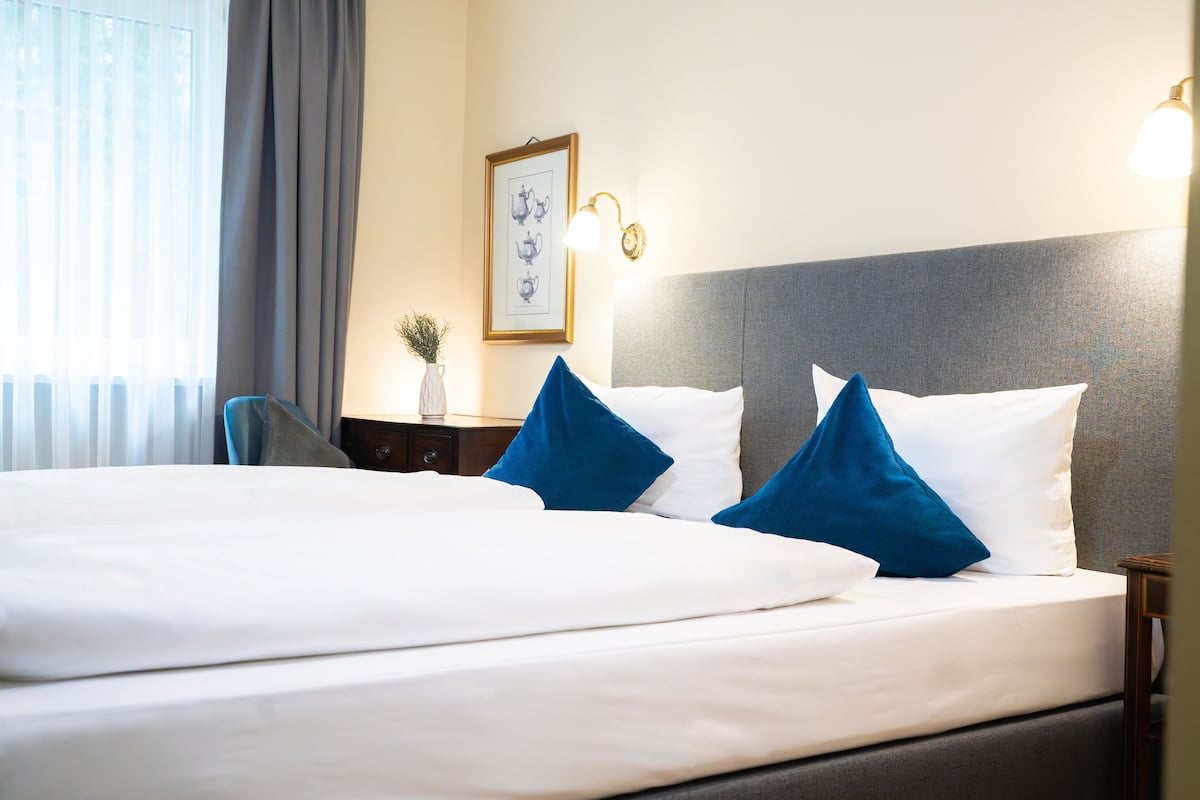 A hotel room with a large bed, a nightstand, a framed picture on the wall, and a lamp.