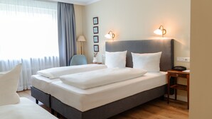 A hotel room with a large bed, bedside tables, a lamp, and a view of the outdoors. - Hotel Altmünchen (Munich)