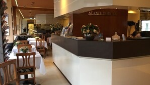 A hotel reception area with a reception desk, chairs, tables, and a large vase of flowers. - Hotel Altmünchen (Munich)