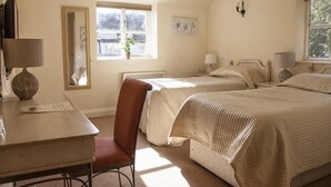 A bedroom with two beds, a desk, and a chair. There is a window providing natural light.