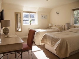 Un dormitorio con dos camas, un escritorio y una silla. Una ventana deja entrar luz natural.