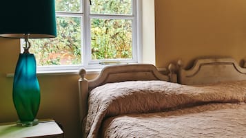 A bedroom with a bed, a bedside table with a lamp, and a window with a view of greenery.