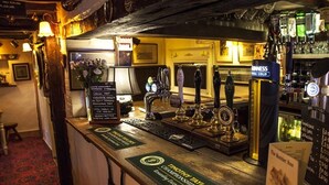 A bar area with a wooden counter, beer taps, and a menu board.