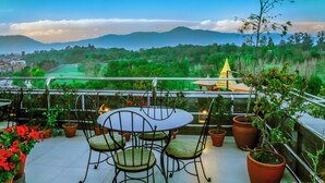 Una terrazza con tavolo e sedie, piante in vaso e vista su una catena montuosa e un tempio.