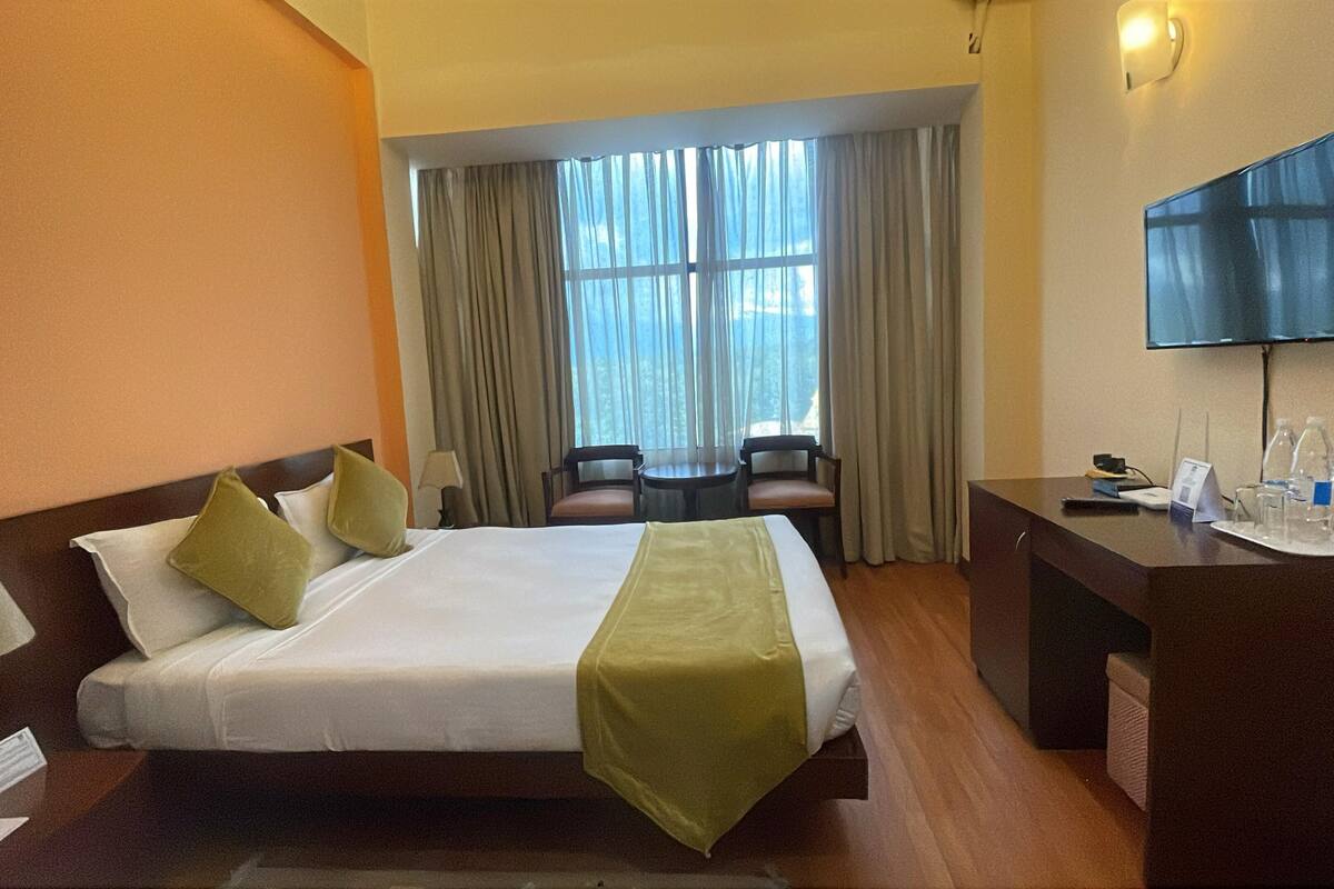 A hotel room with a large bed, two chairs, a desk, and a TV.