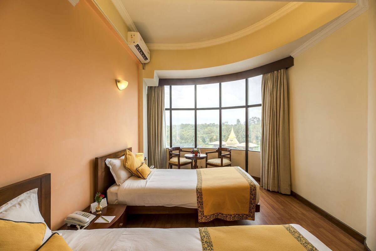 A hotel room with a bed, bedside table, lamp, and a view of a building through large windows.