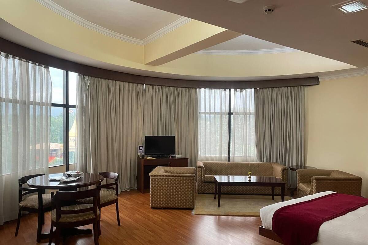 A hotel room with a bed, a sofa, a TV, a dining table with chairs, and a small table with a chair.