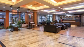 Un'ampia hall con reception, area salotto e piante in vaso.