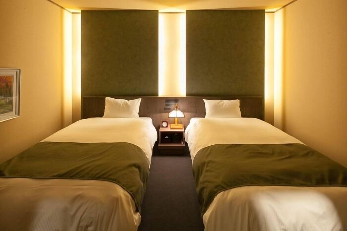 Ein Hotelzimmer mit zwei Einzelbetten, einem Nachttisch mit Lampe und einem gerahmten Bild an der Wand.