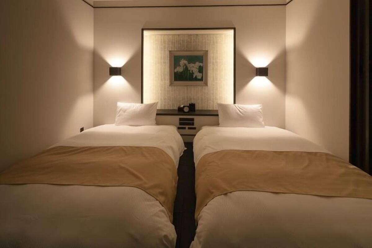 Ein Hotelzimmer mit zwei Betten, einem Nachttisch mit einer Uhr und einem gerahmten Bild an der Wand.