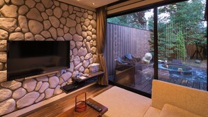 Ein modernes Wohnzimmer mit Steinwand, Flachbildfernseher, Couchtisch aus Holz und einer gemütlichen Couch.