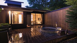 Eine Holzterrasse mit Whirlpool, Kamin aus Stein und Essbereich mit Korbmöbeln.