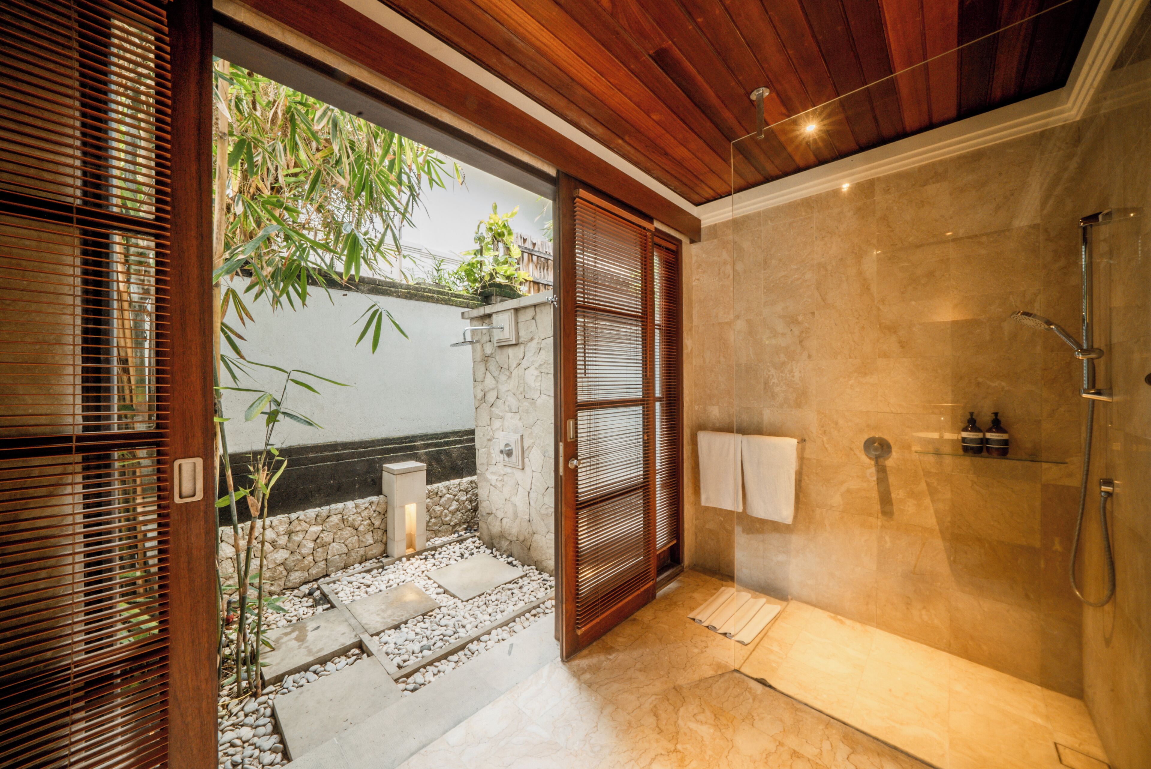 A modern bathroom with a glass-enclosed shower, a stone wall, and a wooden door.