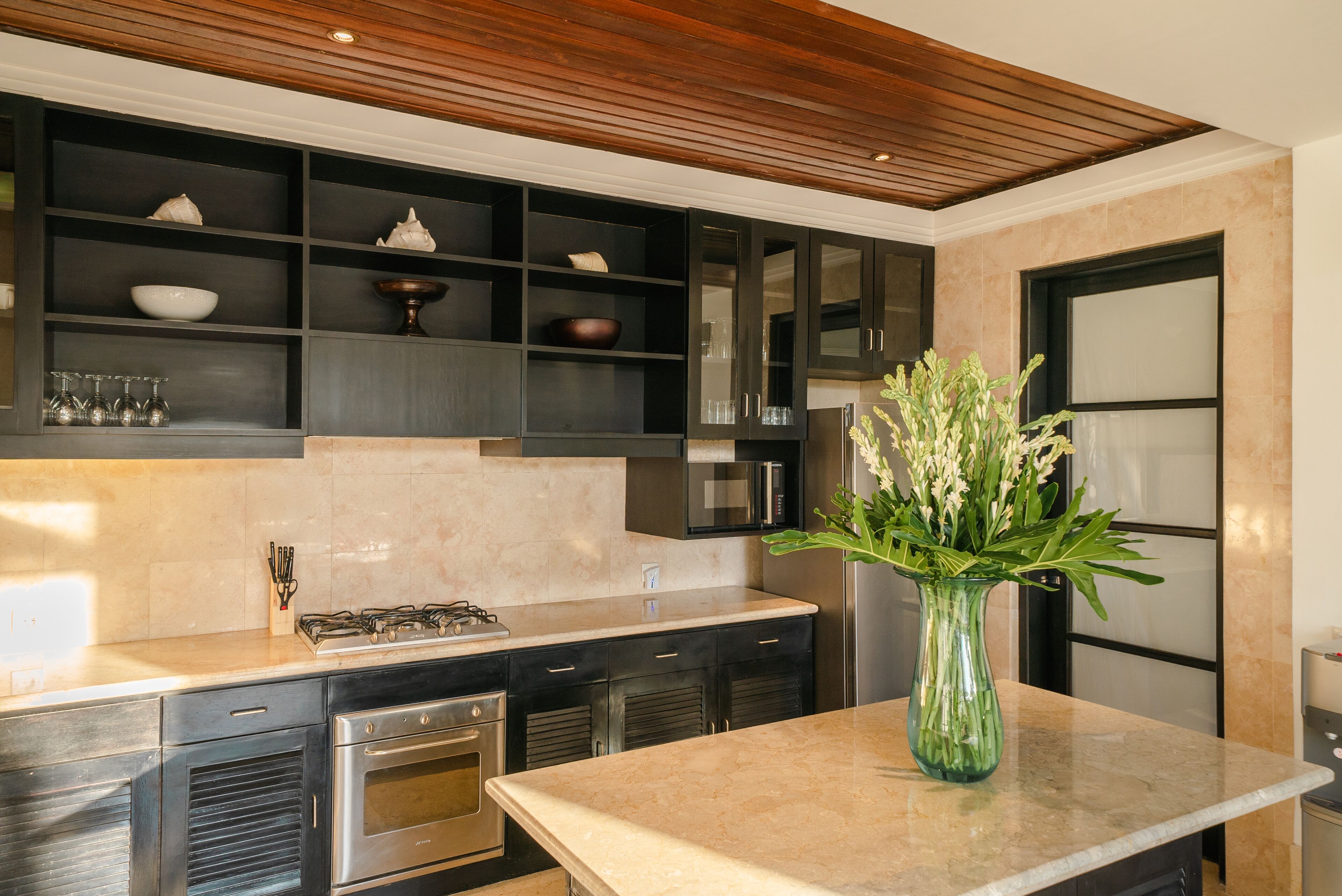 A modern kitchen with dark cabinetry, stainless steel appliances, and a marble countertop.