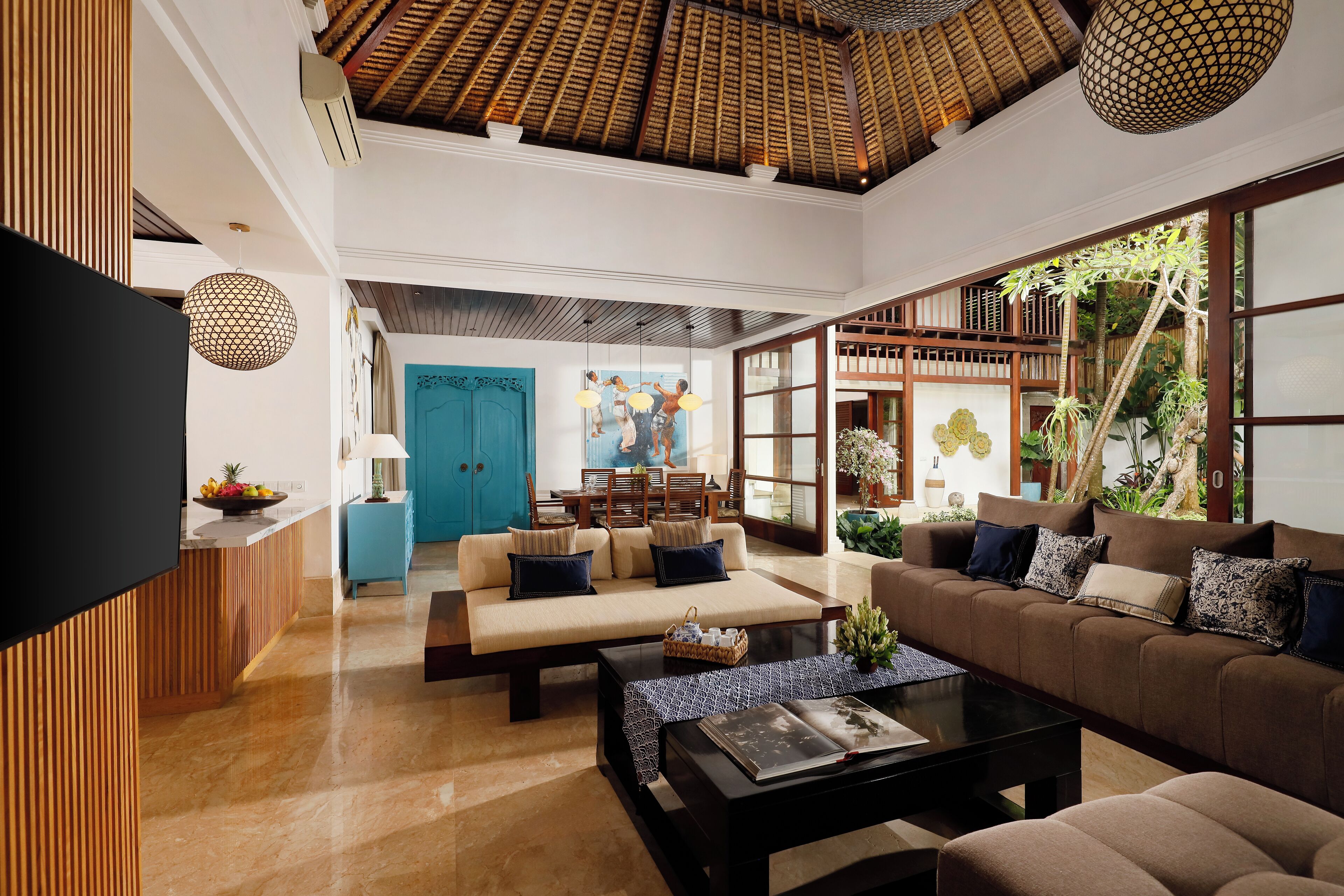 A spacious living area with a high ceiling, a large sofa set, a coffee table, and a TV mounted on the wall.