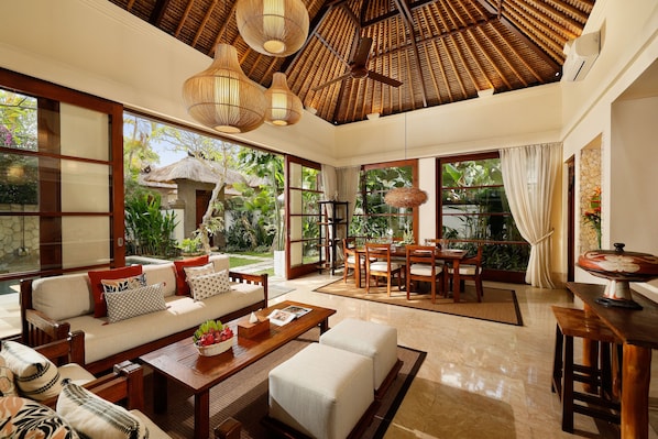 A spacious living area with a wooden ceiling, large windows, and a dining set.