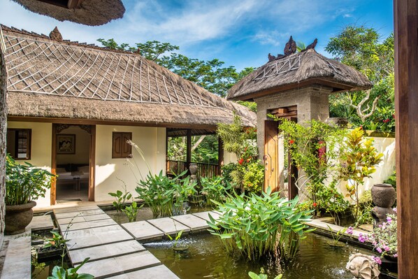 A traditional thatched-roof house with a small garden and a pond.