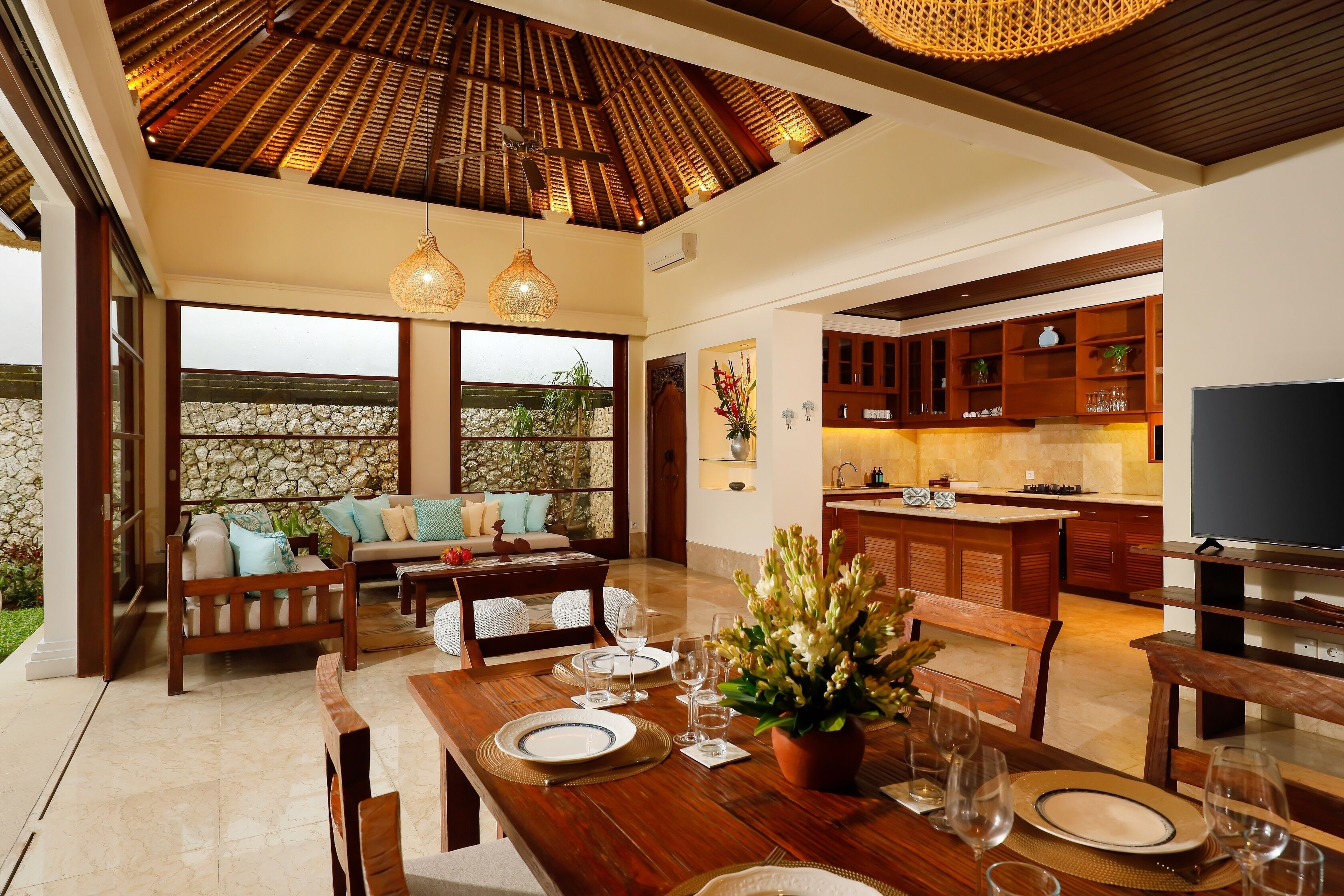 A spacious living area with a dining table set for four, a kitchen with modern appliances, and a stone wall backdrop.