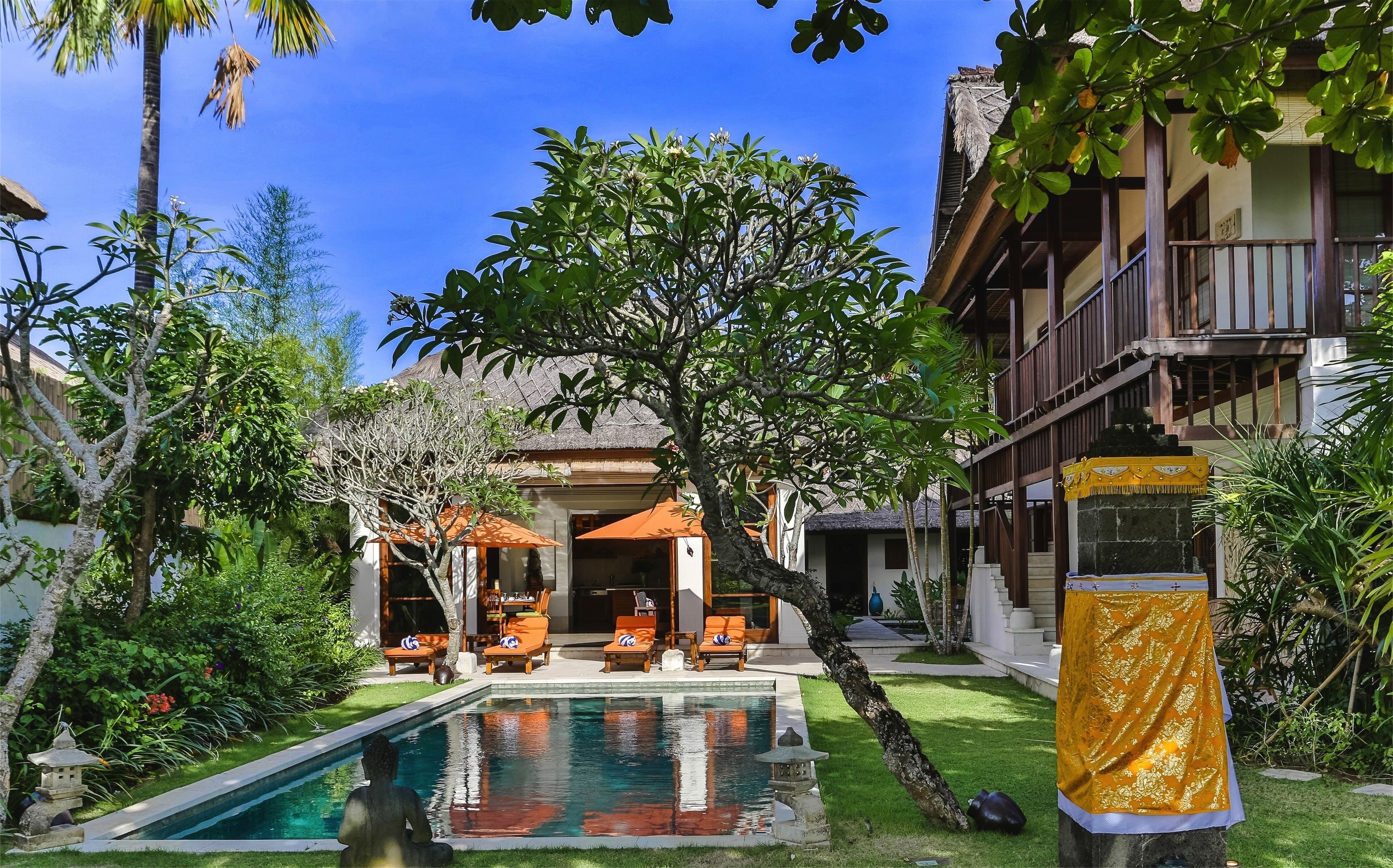 A pool area with lounge chairs, a statue, and a covered seating area.