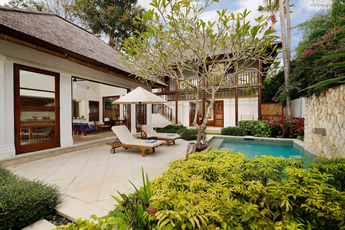 Eine Villa mit Swimmingpool, Liegestühlen und Essbereich.