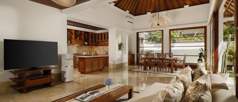 A spacious living room with a flat-screen TV, wooden entertainment unit, and a large sofa with patterned cushions.