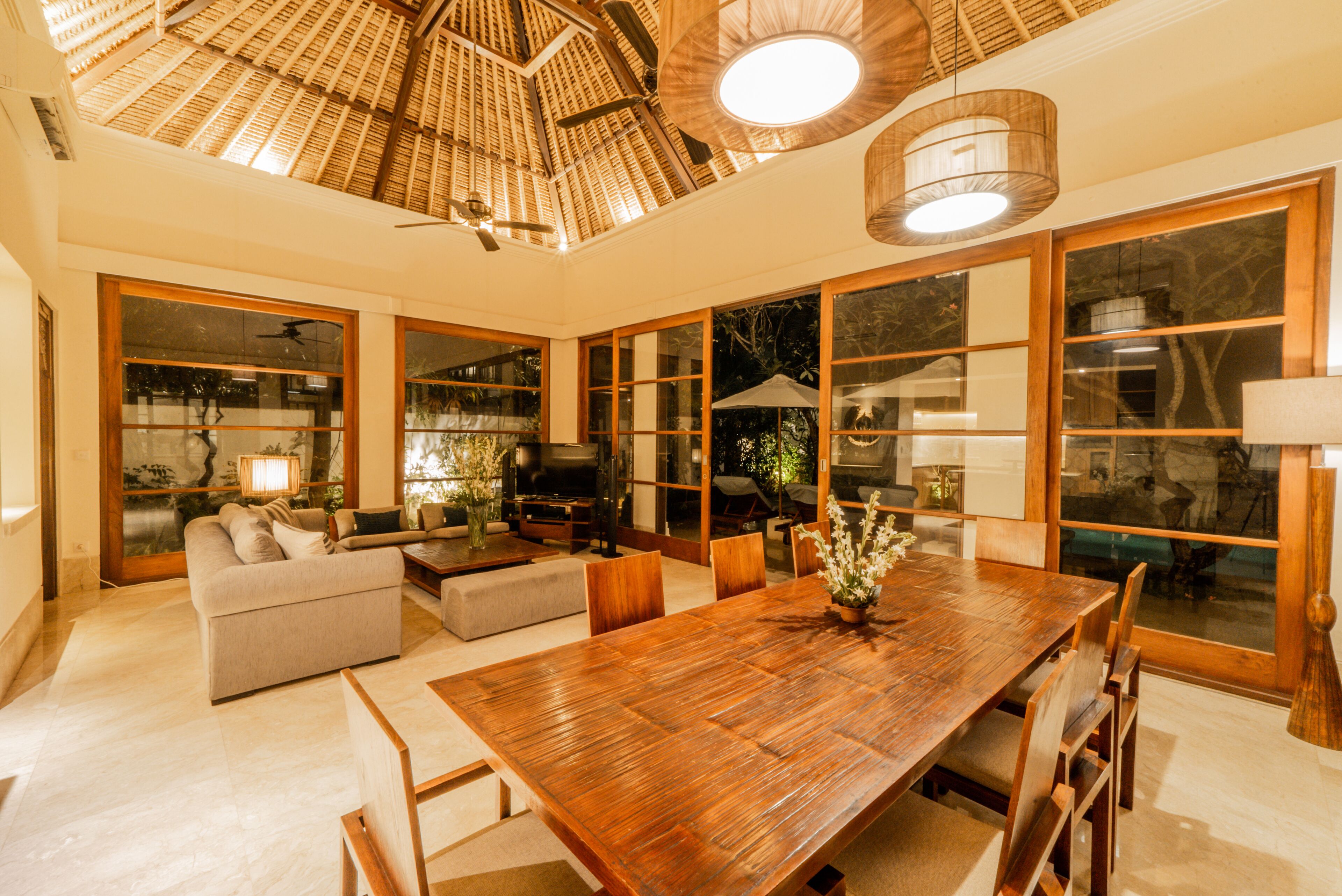 A spacious living area with a large wooden dining table, comfortable seating, and a ceiling fan.