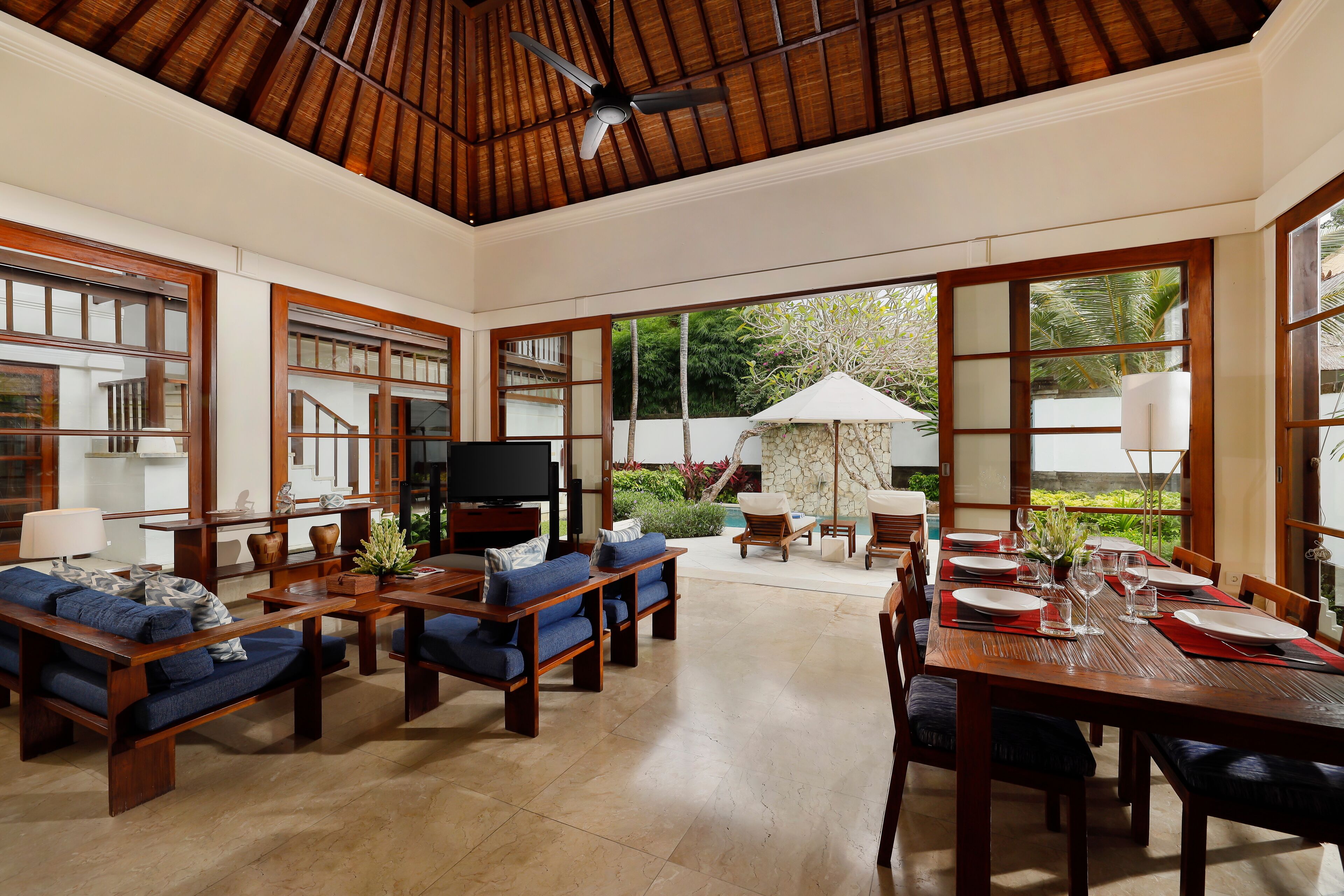 A spacious living area with a large wooden dining table, blue sofas, and a television.