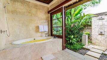 Un baño con una bañera llena de flores amarillas, una ducha y una ventana con vistas a un jardín.