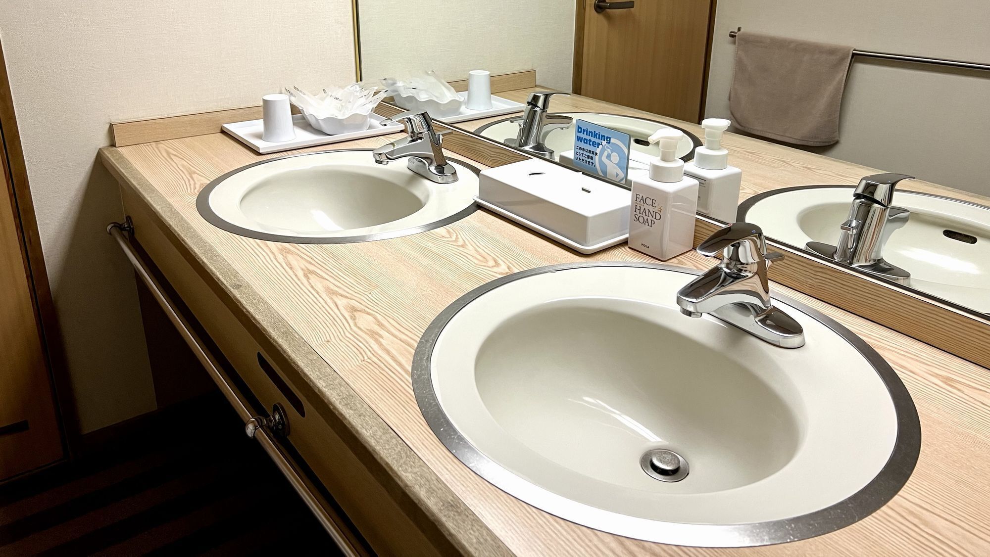 A hotel bathroom with two sinks, a mirror, and amenities like soap and a hand sanitizer dispenser.