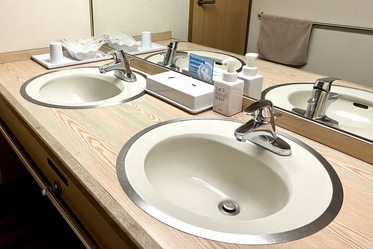 Une salle de bain d’hôtel équipée de deux lavabos, d’un miroir et de produits de première nécessité, comme du savon et un distributeur de gel hydroalcoolique.