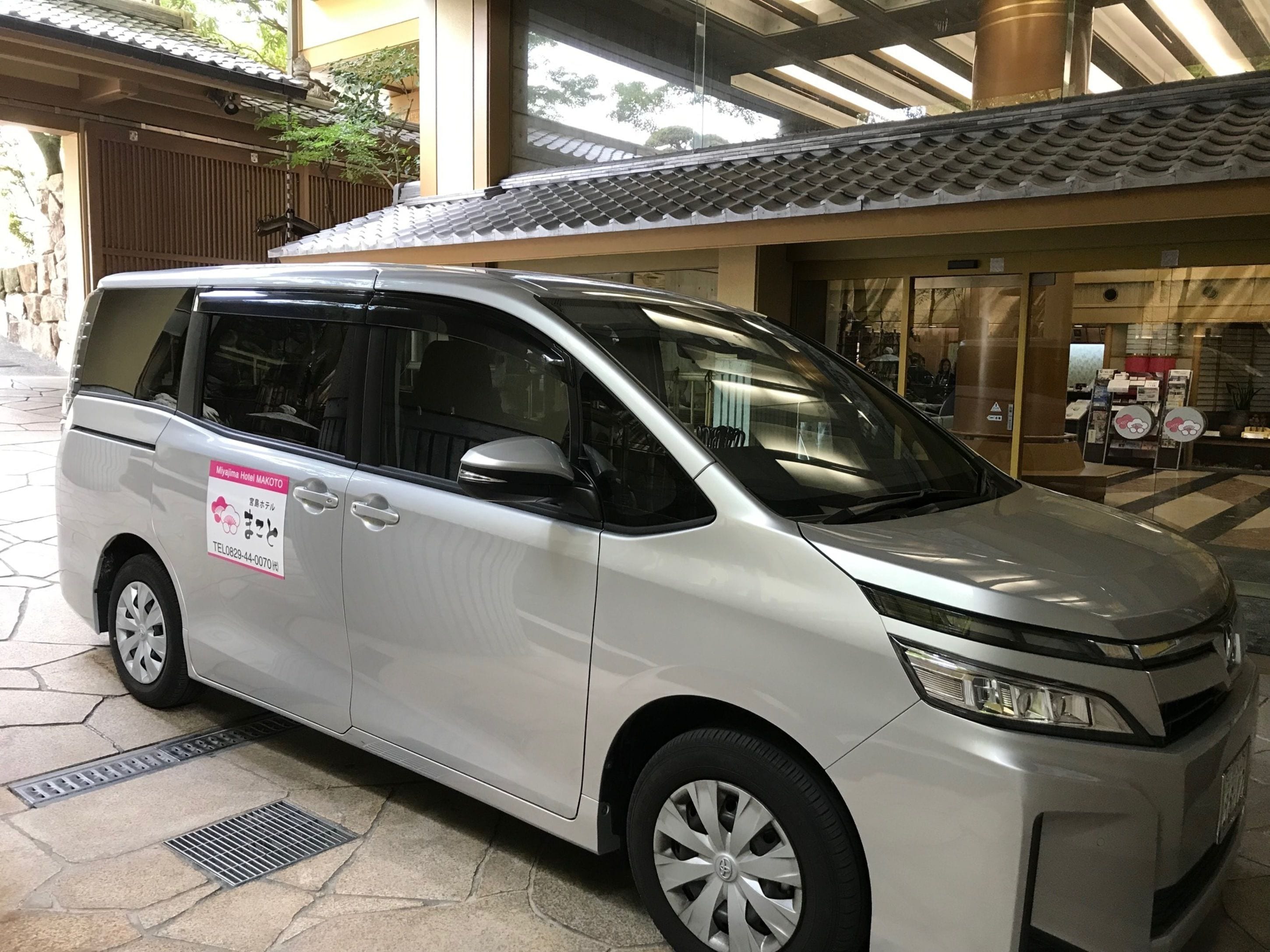 A silver minivan parked outside a building with a tiled roof and a sign indicating it is a hotel.