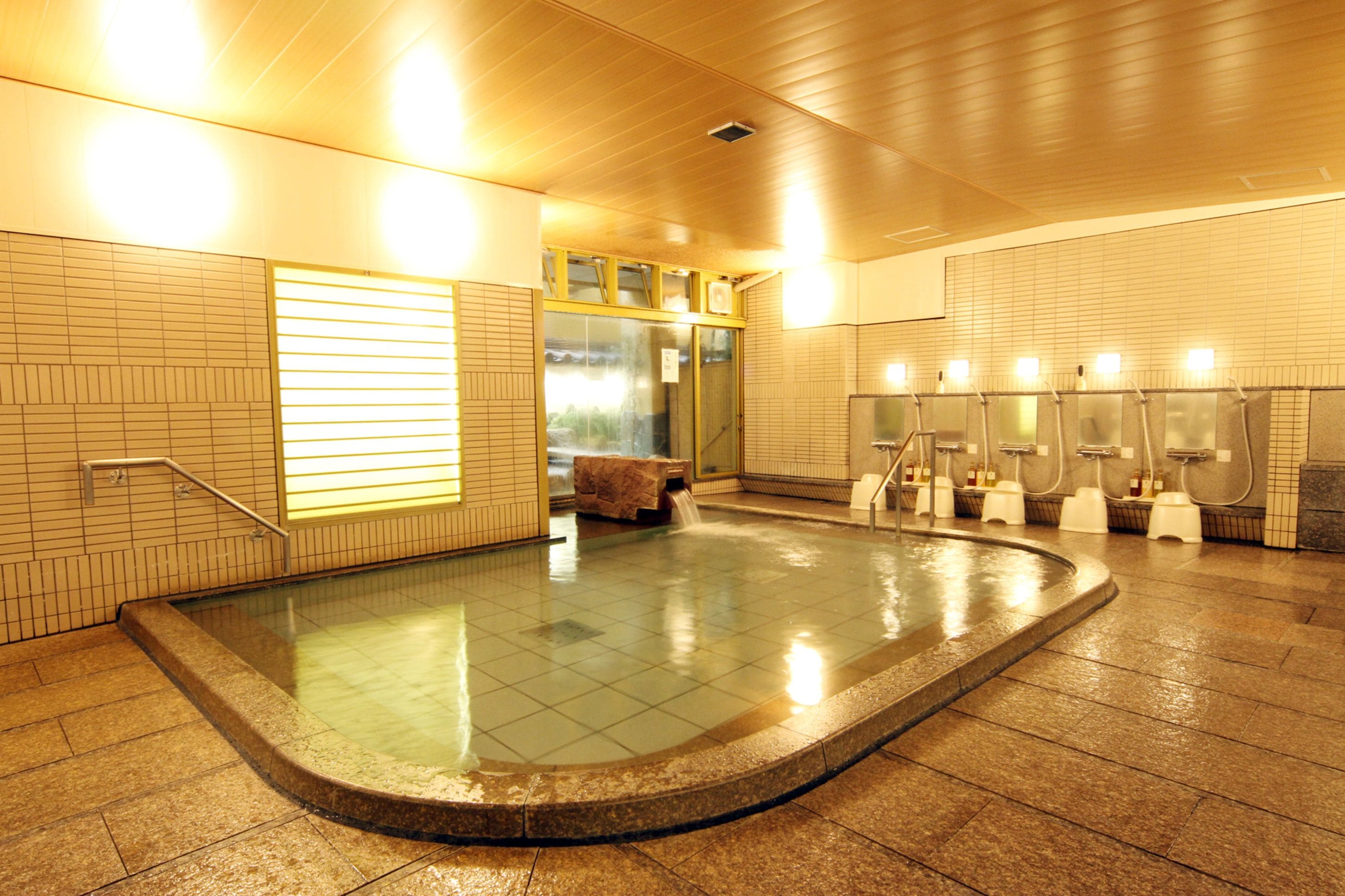 Una amplia piscina interior con suelo de baldosas, un banco y múltiples fuentes de agua.