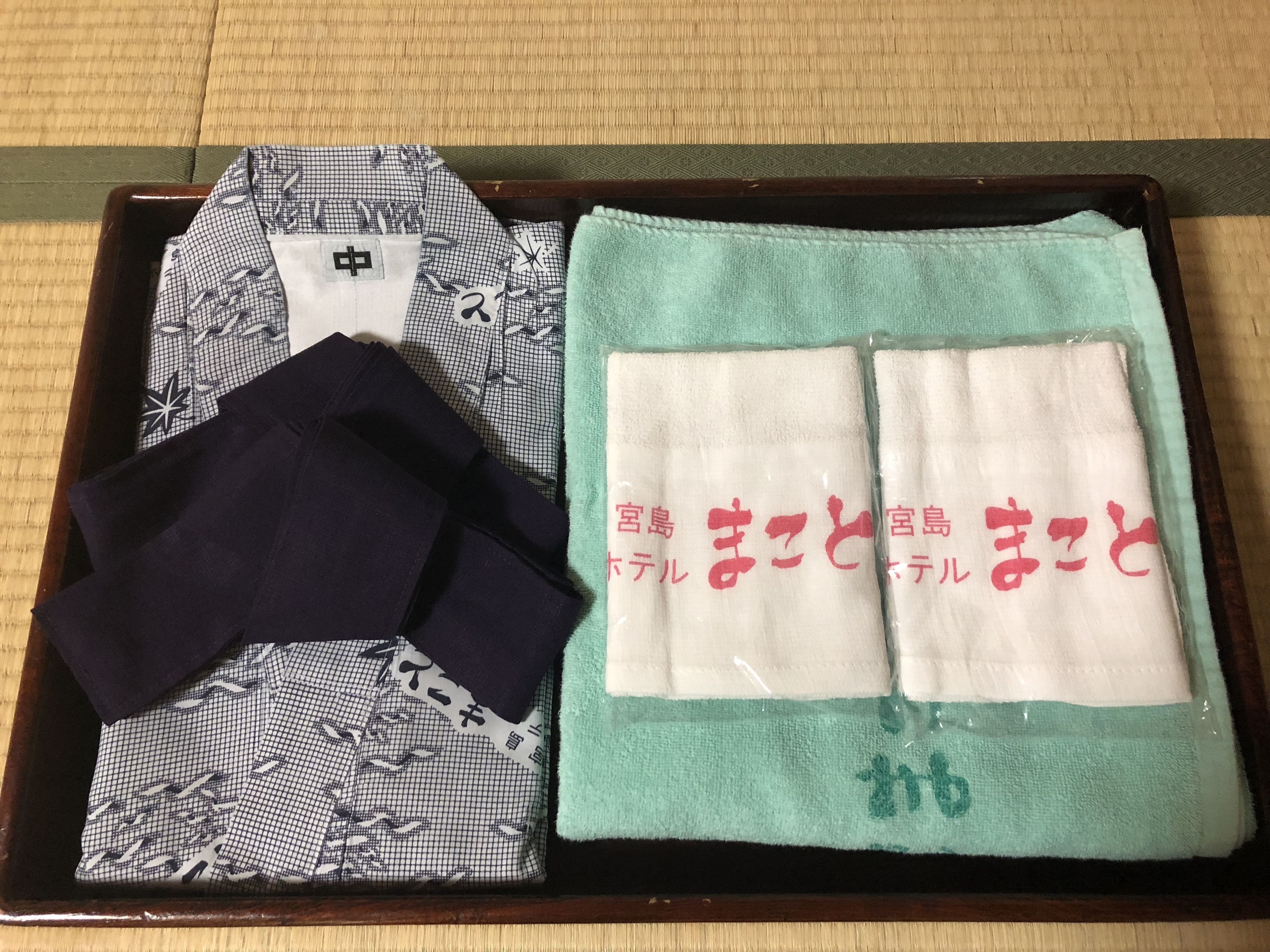 A neatly arranged tray with a patterned cloth, a dark garment, and a light green towel with Japanese text.