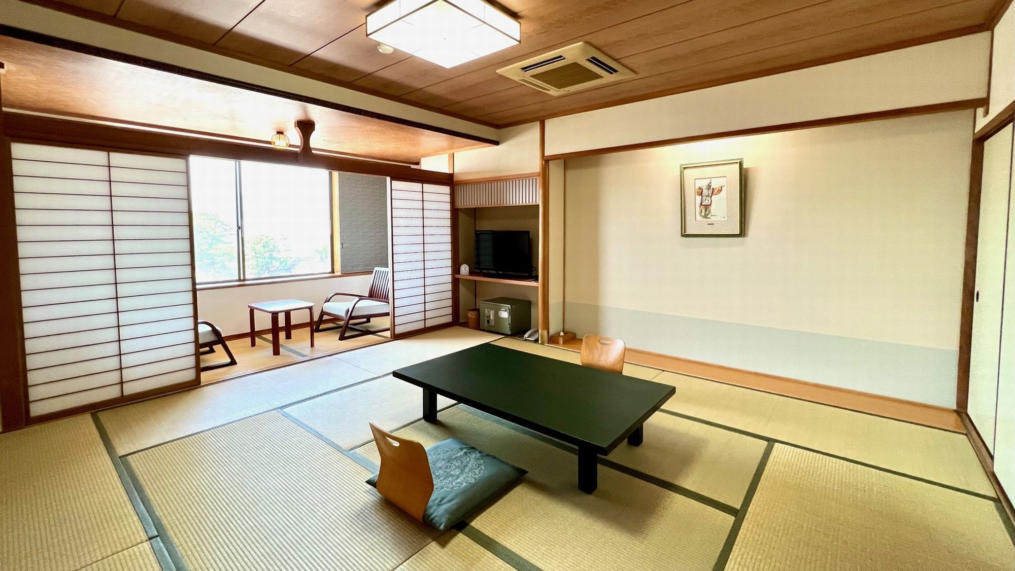 Een kamer met tatami matten, een tatami-tafel, een televisie en een lijst met een afbeelding aan de muur.