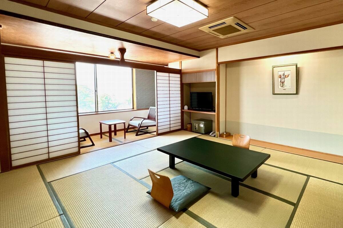 Une pièce avec un sol recouvert de tatamis, une table en tatami, un téléviseur et un tableau encadré accroché au mur.