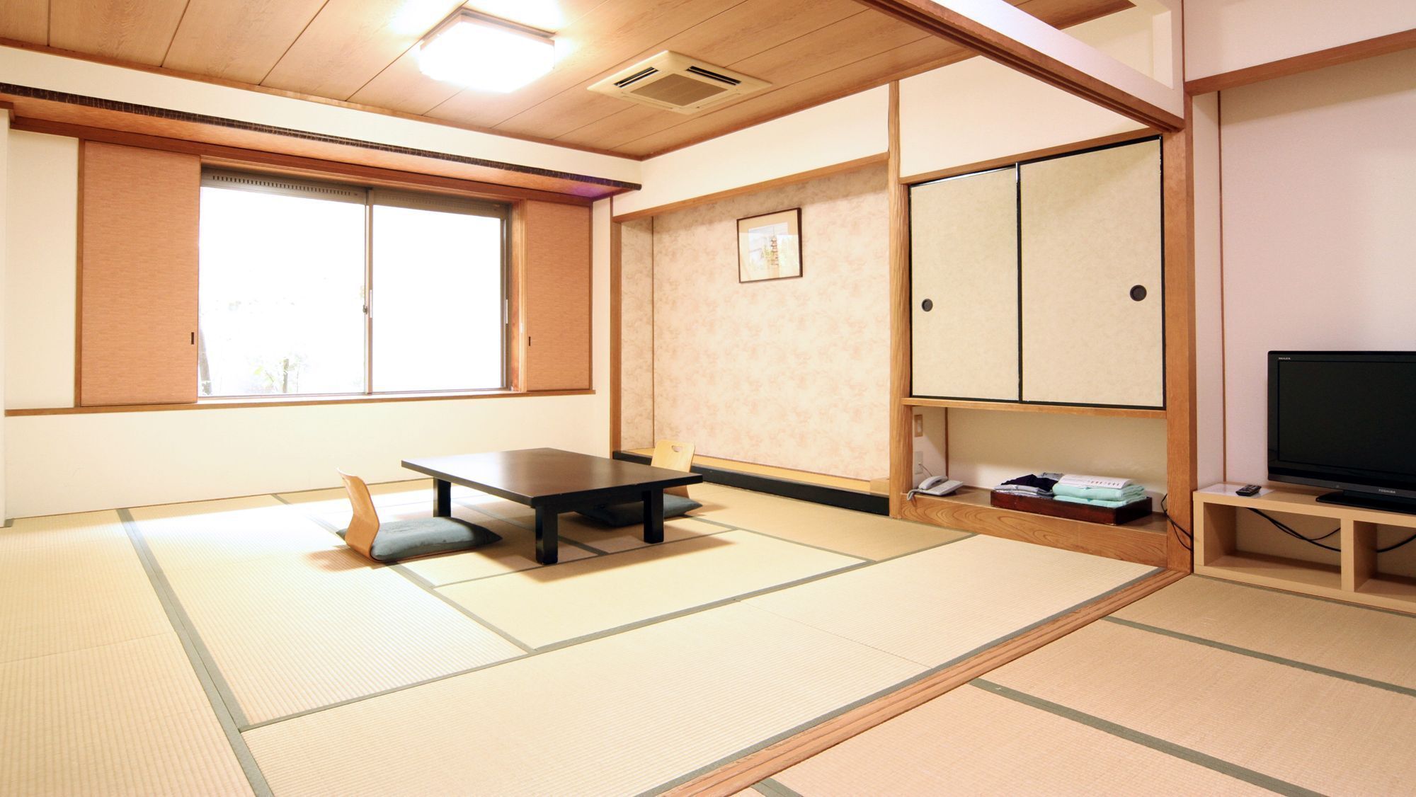 Een kamer met tatami matten, een lage tafel, een televisie en een kast.
