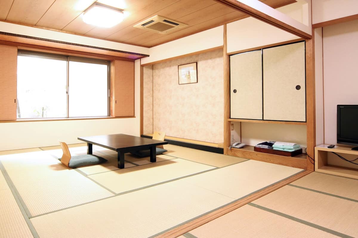 Una habitación con esteras de tatami, una mesa baja, un televisor y un mueble.