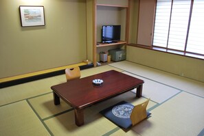 Um quarto japonês tradicional com tatames, uma mesa de madeira baixa e uma televisão numa prateleira.