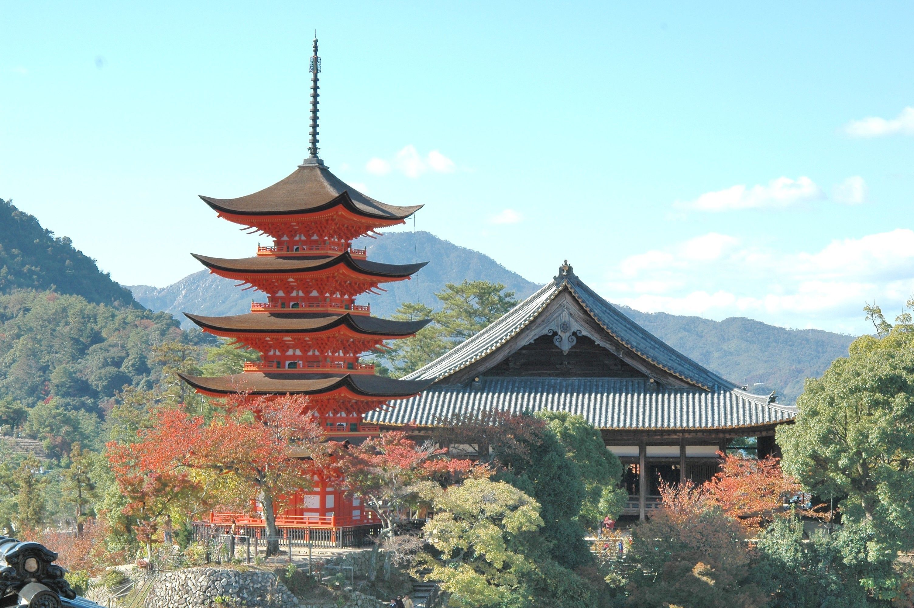 A traditional Japanese pagoda with multiple tiers, surrounded by autumn foliage and a mountain backdrop.