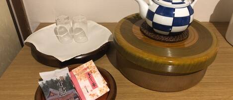Una mesa de madera con una tetera azul y blanca a cuadros, dos vasos transparentes, una bandeja blanca con un paño y una bandejita con una bolsita de té y una imagen.