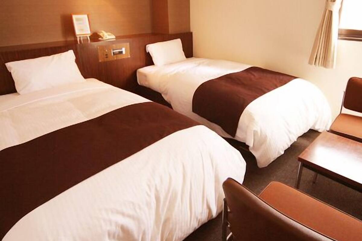 A hotel room with two beds, a bedside table with a lamp, and a chair.
