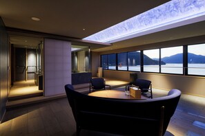 A modern room with a large window overlooking a body of water and mountains. There is a round table with chairs and a small wooden cabinet. - Itsukushima Iroha  (Hatsukaichi)